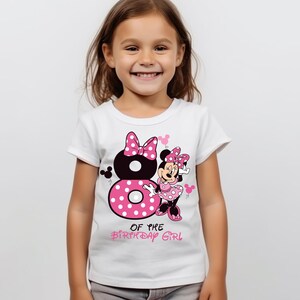 K&ouml;nnte beinhalten: Wei&szlig;es T-Shirt mit einem Minnie Mouse-Motiv. Das Design umfasst eine gro&szlig;e, rosa gepunktete Zahl 8, Minnie Mouse und den Text "OF THE BIRTHDAY GIRL". Das T-Shirt ist f&uuml;r ein Kind.