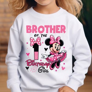 May include: White sweatshirt with a pink Minnie Mouse graphic. The design includes the text "Brother of the Birthday Girl" and the number "1". Minnie Mouse is wearing a pink dress and bow. The design also features pink bows and stars.
