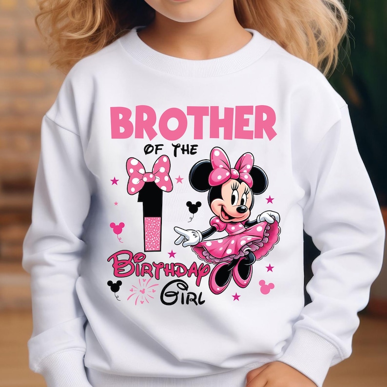 May include: White sweatshirt with a pink Minnie Mouse graphic. The design includes the text "Brother of the Birthday Girl" and the number "1". Minnie Mouse is wearing a pink dress and bow. The design also features pink bows and stars.