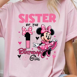 May include: Pink t-shirt featuring a Minnie Mouse graphic. The design includes the text "SISTER OF THE 1 BIRTHDAY GIRL" in pink and black, along with Minnie Mouse in a pink dress and bow. Pink stars and Mickey Mouse icons are also present.