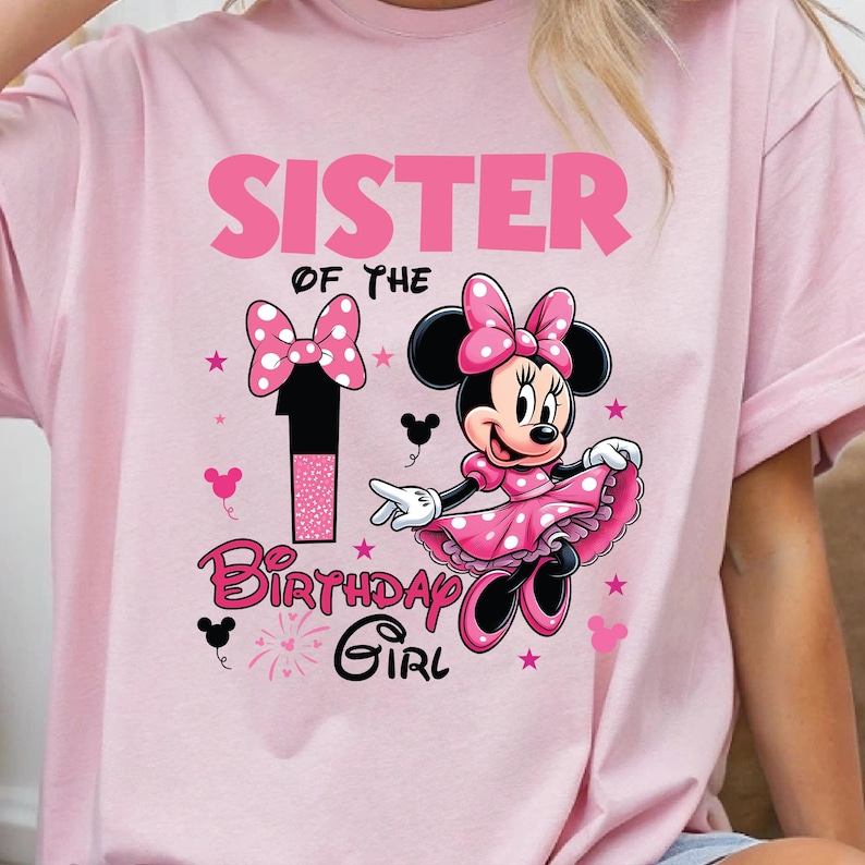 May include: Pink t-shirt featuring a Minnie Mouse graphic. The design includes the text "SISTER OF THE 1 BIRTHDAY GIRL" in pink and black, along with Minnie Mouse in a pink dress and bow. Pink stars and Mickey Mouse icons are also present.
