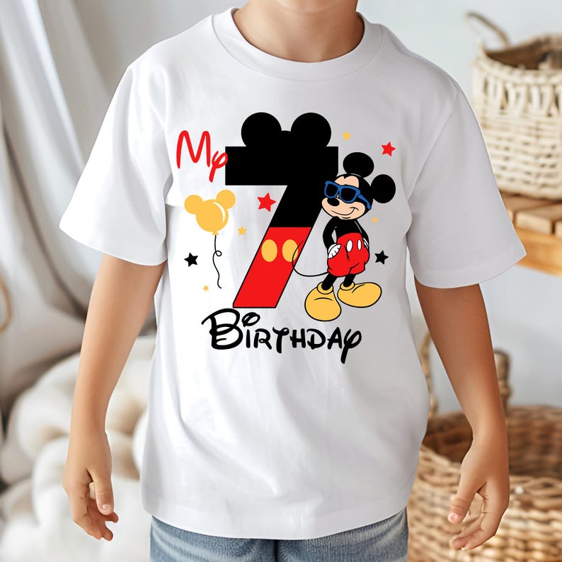 May include: White t-shirt featuring a graphic of Mickey Mouse wearing sunglasses, with the number 7 in red and black, and the words "My Birthday". The design includes stars and a yellow balloon.