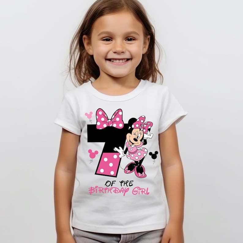 K&ouml;nnte beinhalten: Wei&szlig;es T-Shirt mit einem Minnie Mouse-Design. Das Design umfasst eine gro&szlig;e schwarze Zahl 7 mit rosa Punkten, eine rosa Schleife und den Text "OF THE BIRTHDAY GIRL". Das T-Shirt ist f&uuml;r ein Kind.