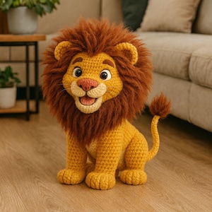 May include: A crocheted lion toy with a golden yellow body and a brown mane. The lion has a pink nose and a smiling expression. The toy is sitting on a wooden floor. The lion has a small tail.