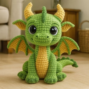 以下が含まれることがあります： 緑と黄色の手作りの編み物ドラゴン。ドラゴンは大きな黒い目、黄色の角、翼を持っています。木製の床に座っています。ドラゴンは約20cmの高さです。