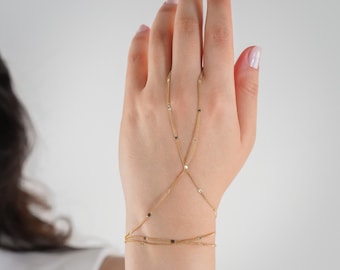 Puede incluir: Pulsera de cadena de mano dorada. Esta delicada pieza presenta finas cadenas que conectan una pulsera de muñeca con un anillo para el dedo. La pulsera está adornada con pequeños detalles redondos y está diseñada para usarse en el dorso de la mano.