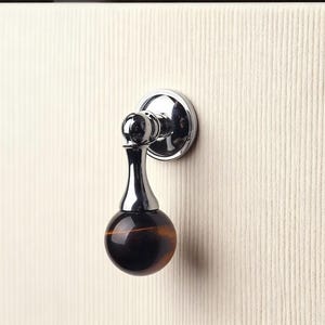 以下が含まれることがあります： 丸みを帯びた磨かれた茶色と黒のオーブが付いた、クロムと茶色のキャビネットプル。 プルは、クリーム色のテクスチャードキャビネットドアに取り付けられています。 ハードウェアはモダンでエレガントなデザインです。