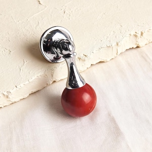 May include: A cabinet pull with a polished chrome finish and a round, glossy red knob. The pull has a decorative design and is mounted on a circular base. This hardware is suitable for drawers and cabinets.