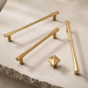 May include: Three gold-toned metal cabinet pulls and one matching square cabinet knob. The pulls feature a long, slender bar design with hexagonal ends and the name Nicole engraved in a script font on the center of the bar surface.
