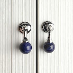 May include: Two cabinet pulls with a polished chrome finish and a deep blue, spherical stone. The pulls are mounted on a white, vertically-grooved surface, suggesting a cabinet door.