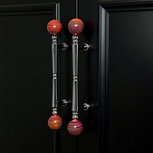 Könnte beinhalten: Zwei Schranktürgriffe mit polierter Chromoberfläche und farbenfrohen, gestreiften kugelförmigen Akzenten. Die Griffe sind an einer schwarzen Schranktür montiert. Die kugelförmigen Akzente haben rote, orange, gelbe und blaue Streifen.