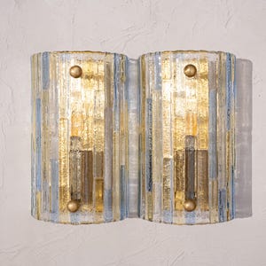 May include: A pair of wall sconces featuring vertical, textured glass panels in shades of clear, gold, and light blue. Each rectangular fixture is secured with two circular, brass-toned metal knobs positioned at the top and bottom centres.