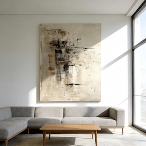 May include: Large abstract painting with a neutral color palette of beige, brown, and black. The artwork features a textured surface with brushstrokes and geometric shapes. The painting hangs above a gray sectional sofa and a wooden coffee table.