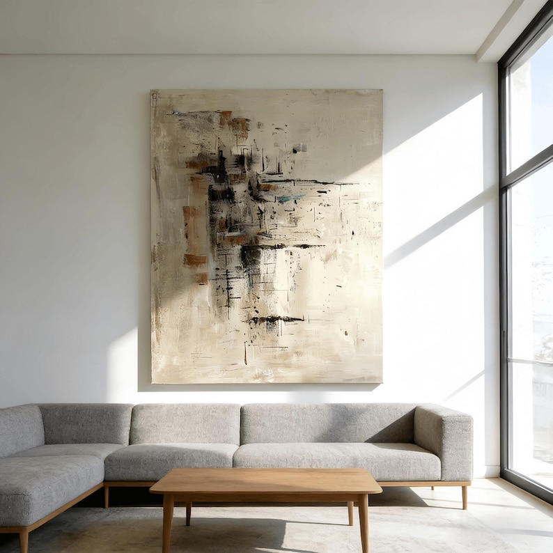 May include: Large abstract painting with a neutral color palette of beige, brown, and black. The artwork features a textured surface with brushstrokes and geometric shapes. The painting hangs above a gray sectional sofa and a wooden coffee table.