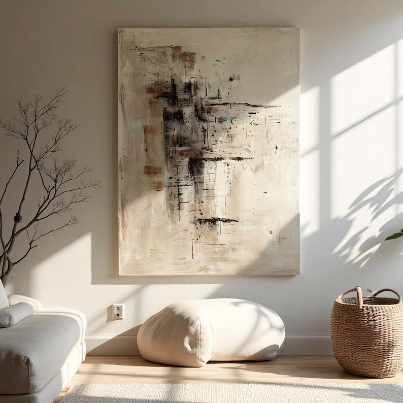 May include: Large abstract painting with beige, brown, and black brushstrokes. The artwork hangs on a white wall, complemented by a neutral-toned interior with a beige ottoman, a woven basket, and a sofa.