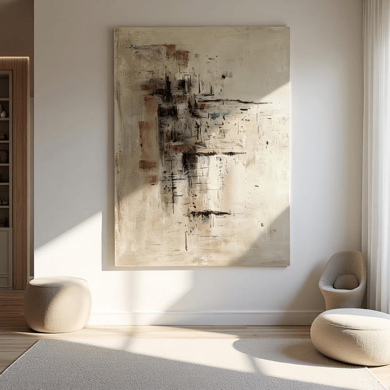 May include: Large abstract painting with beige, brown, and black brushstrokes. The artwork hangs on a white wall in a well-lit room. Two beige ottomans and a chair are in front of the painting.