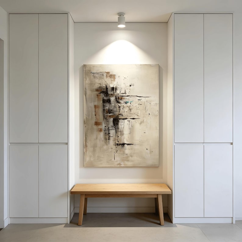 May include: An abstract painting with beige, brown, and black brushstrokes hangs above a wooden bench. The artwork is centered on a white wall, flanked by two white storage cabinets. The room is well-lit with a ceiling spotlight.