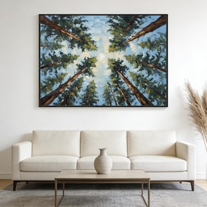Puede incluir: Una pintura al óleo de árboles altos que se elevan hacia un cielo azul, vista desde abajo. La obra de arte está enmarcada en negro y cuelga sobre un sofá blanco. La pintura captura la perspectiva de mirar hacia arriba a través de un dosel forestal.