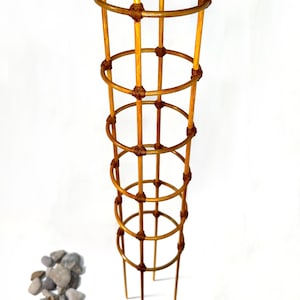 Peut inclure: Un treillis pour plantes cylindrique et haut, composé de tiges en bois brun clair disposées en grille verticale. La structure présente plusieurs anneaux circulaires fixés aux supports verticaux par des nœuds en ficelle brun foncé.