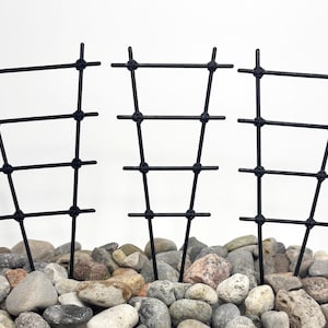 May include: Three black metal plant supports with a grid design. The supports are placed in a bed of gray and tan river rocks. The supports are designed to help plants grow vertically.