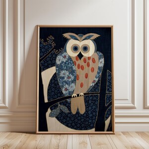 May include: Framed artwork depicting a stylized owl on a branch. The owl has large, round eyes and a patterned body with blue, beige, and red accents. The background is a dark blue with floral patterns, and the frame is a light brown.