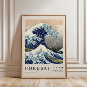 May include: A framed print of Hokusai's "The Great Wave off Kanagawa." The artwork depicts a large, stylized wave in shades of blue and white, with Mount Fuji in the background. The print includes the artist's name and title in English and Japanese.