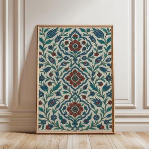 Puede incluir: Impresión artística enmarcada con un diseño floral simétrico en rojo, azul y verde sobre un fondo crema. La obra de arte está enmarcada en un marco de madera marrón claro. La impresión se muestra contra una pared blanca.