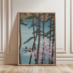 May include: Framed art print depicting a serene lake scene. Tall, slender trees frame the view of a boat on the water. Pink flowering branches add a touch of color against the blue water and sky. The artwork is in a wooden frame.