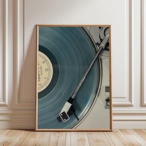 Könnte beinhalten: Gerahmter Druck mit einer Nahaufnahme eines Vintage-Plattenspielers mit einer blauen Schallplatte. Das Etikett der Schallplatte ist sichtbar, mit dem Text "Taylor Swift - Midnights 2". Der Plattenspielerarm ist über der Schallplatte positioniert. Der Rahmen ist hellbraun.