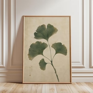 May include: A framed vertical wall art print featuring a botanical illustration of a ginkgo branch with four dark green, fan-shaped leaves against a textured, light beige background. The lower left corner contains small, vertical black Chinese text.