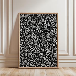 May include: Abstract art print in a wooden frame. The artwork features a repeating pattern of white, stylized shapes against a black background. The shapes have a raised, textured appearance, creating a 3D effect. The print is displayed against a white wall and wooden floor.