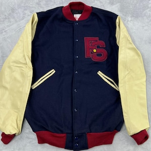 May include: A navy blue varsity jacket with cream-colored leather sleeves. The jacket features a red collar, cuffs, and a large red embroidered "FS" logo on the chest. It has a button-up front and two front pockets with cream-colored trim.