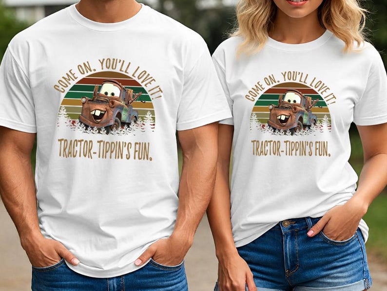 May include: A white short-sleeved t-shirt featuring a graphic of a brown tow truck character. The design includes a sunset background with green and orange stripes, pine trees, and the text: COME ON, YOU'LL LOVE IT! TRACTOR-TIPPIN'S FUN.