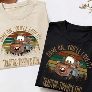 May include: A beige t-shirt and a black t-shirt, each featuring a graphic of a rusty tow truck character. The design includes a sunset background with horizontal stripes, pine trees, and the text "COME ON, YOU'LL LOVE IT! TRACTOR-TIPPIN'S FUN."