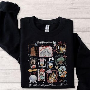 May include: Black sweatshirt featuring a colorful graphic of Disney characters and landmarks. The design includes Mickey Mouse, Donald Duck, and Cinderella's castle, with the text "Walt Disney World" and "2026". The phrase "The Most Magical Place on Earth" is also included.