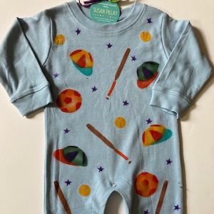 May include: A light blue baby onesie with a baseball theme. The onesie features a pattern of baseball bats, baseballs, and baseball caps in various colors. The text "Susan Pillay" is printed on the onesie.