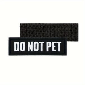 May include: A black rectangular patch with the white text "DO NOT PET". The patch is above a dark gray rectangular piece of fabric. The text is in a bold, sans-serif font.