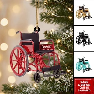 Peut inclure: Un ornement en forme de fauteuil roulant rouge avec un siège et un dossier noirs, portant le nom DAVID imprimé en blanc sur le cadre latéral. L'ornement est suspendu par une ficelle dorée et comporte une attache circulaire noire au sommet.