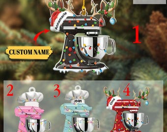 May include: Christmas ornament shaped like a stand mixer, with a reindeer antler design. The ornament is available in black, pink, blue, and red. Each mixer has a chef's hat and is decorated with Christmas lights. The text "Annamarie", "Joan", and "Oma" are visible.