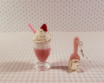 May include: A pair of novelty earrings and a milkshake. The earrings are shaped like a spoon with whipped cream. The milkshake is pink with whipped cream, a strawberry, and a pink straw. The items are on a pink and white checkered surface.
