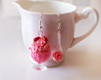 May include: A pair of whimsical earrings. One earring is a miniature pink sundae with whipped cream and a strawberry. The other is a clear spoon with a pink rose. Both earrings have silver-colored hooks.