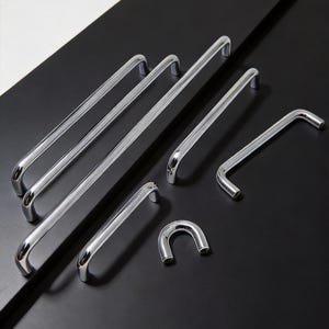 May include: A collection of polished chrome door handles in various shapes and sizes. The handles are arranged on a black surface, showcasing their reflective quality. The designs include straight bars, curved handles, and a U-shaped pull.
