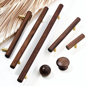 Könnte beinhalten: Eine Auswahl an Holzmöbelbeschlägen, darunter verschiedene Größen von Griffen, Knöpfen und eine runde Kugel. Die Griffe sind dunkelbraun mit messingfarbenen Befestigungen. Die Knöpfe und die Kugel sind ebenfalls dunkelbraun.