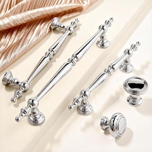 Op de afbeelding: Een verzameling gepolijste chromen kastbeslagen, waaronder verschillende handgrepen en twee knopstijlen. De handgrepen variëren in lengte en alle onderdelen hebben een reflecterend, glanzend oppervlak. De hardware is gerangschikt op een licht oppervlak.