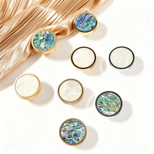 Peut inclure: Une collection de boutons de meubles ronds avec divers motifs. Certains boutons présentent des incrustations d'ormeau irisé, tandis que d'autres ont un aspect nacré blanc. Les boutons ont des bords en métal doré, argenté et bronze.