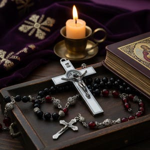 Peut inclure: Nature morte religieuse avec un crucifix blanc orné d'une figurine de Jésus en argent, un chapelet avec des perles noires et rouges, et une bougie allumée dans un porte-bougie en laiton. Un livre avec des lettres dorées et un tissu violet sont également présents.