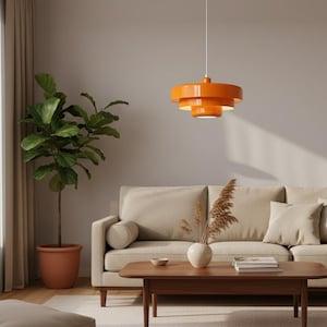 Könnte beinhalten: Eine orangefarbene, mehrstufige Pendelleuchte hängt über einem Wohnzimmer. Der Raum verfügt über ein beiges Sofa, einen Holztisch und eine große Topfpflanze. Die Leuchte ist der Mittelpunkt und wirft ein warmes Licht.