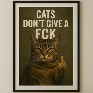 Könnte beinhalten: Gerahmter Druck mit einer getigerten Katze, die den Mittelfinger zeigt. Der weiße Text über der Katze lautet "CATS DON'T GIVE A FCK". Die Katze hat grüne Augen und befindet sich vor einem dunkelgrünen Hintergrund. Eine Kugel aus braunem Garn liegt auf einer Holzoberfläche.
