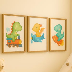 Könnte beinhalten: Drei gerahmte Kunstdrucke mit Dinosaurier-Illustrationen. Ein Dinosaurier fährt Zug, ein anderer fliegt im Flugzeug und der dritte auf einer Rakete. Die Drucke sind in hellen Holzrahmen und werden an einer cremefarbenen Wand gezeigt.