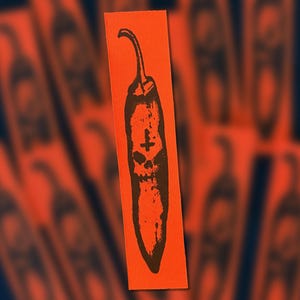 Pode incluir: Um emblema retangular de tecido em laranja brilhante com um gráfico serigrafado a preto de uma malagueta. O design da malagueta incorpora um motivo de caveira no centro e um pequeno símbolo de cruz posicionado acima da caveira.